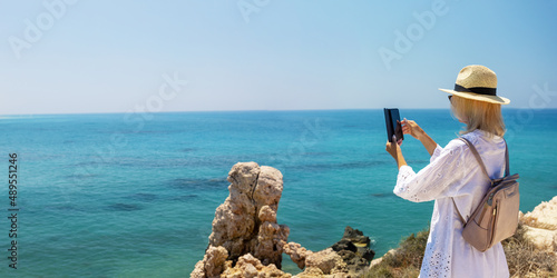 Woman traveler taking photo with mobile phone in the beach. Banner with copy space.