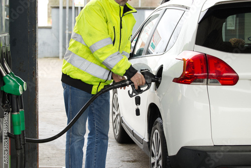 Close-up of the adult caucasian men's hand refilling diesel into the white car at the petrol station. self service refueling concept