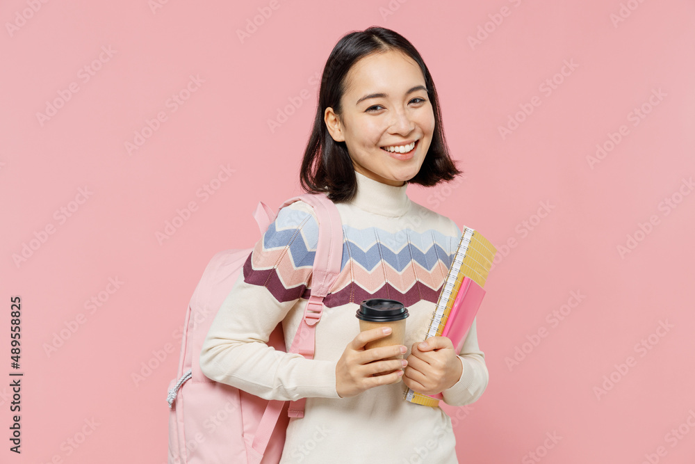 Teen student girl of Asian ethnicity wearing sweater backpack hold books hold takeaway delivery craft cup coffee to go isolated on pastel plain pink background Education in university college concept Teen student girl of Asian ethnicity wearing sweater backpack hold books hold takeaway delivery craft cup coffee to go isolated on pastel plain pink background Education in university college concept