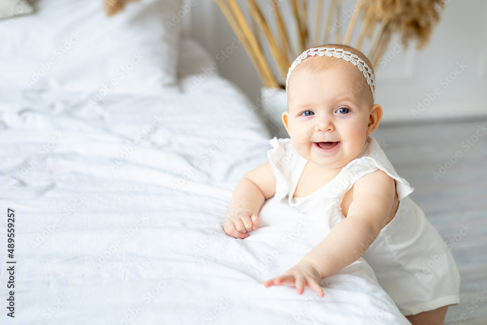 cute little baby in white cotton bodysuit smiling or laughing, baby girl on a light bed at home in the nursery close-up cute little baby in white cotton bodysuit smiling or laughing, baby girl on a light bed at home in the nursery close-up