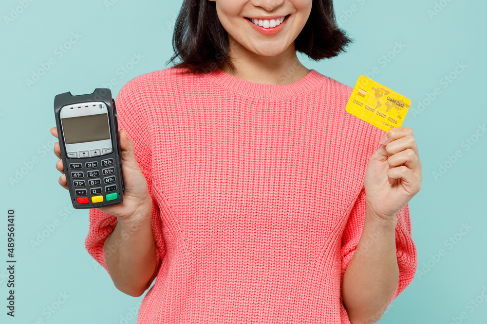 Close up cropped young woman of Asian ethnicity 20s in pink sweater hold wireless modern bank payment terminal to process acquire credit card payments isolated on pastel plain light blue background. Close up cropped young woman of Asian ethnicity 20s in pink sweater hold wireless modern bank payment terminal to process acquire credit card payments isolated on pastel plain light blue background.
