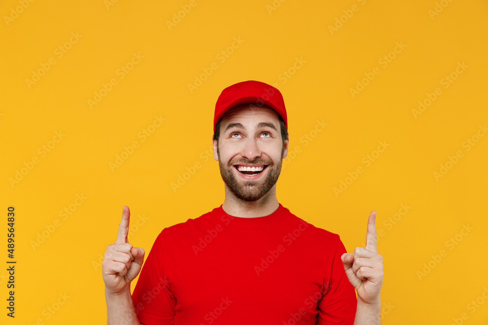 Professional fun delivery guy employee man in red cap T-shirt uniform workwear work as dealer courier point index finger overhead on workspace area isolated on plain yellow background Service concept.