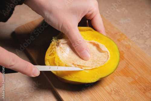 Close-up of woman's hands cutting fresh mango on wooden cutting board at home kitchen