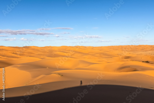 Shadow of the photographer in Sahara Desert landscape On the top of the sand dune shooting the golden yellow vast sand dunes and cloudy blue sky.