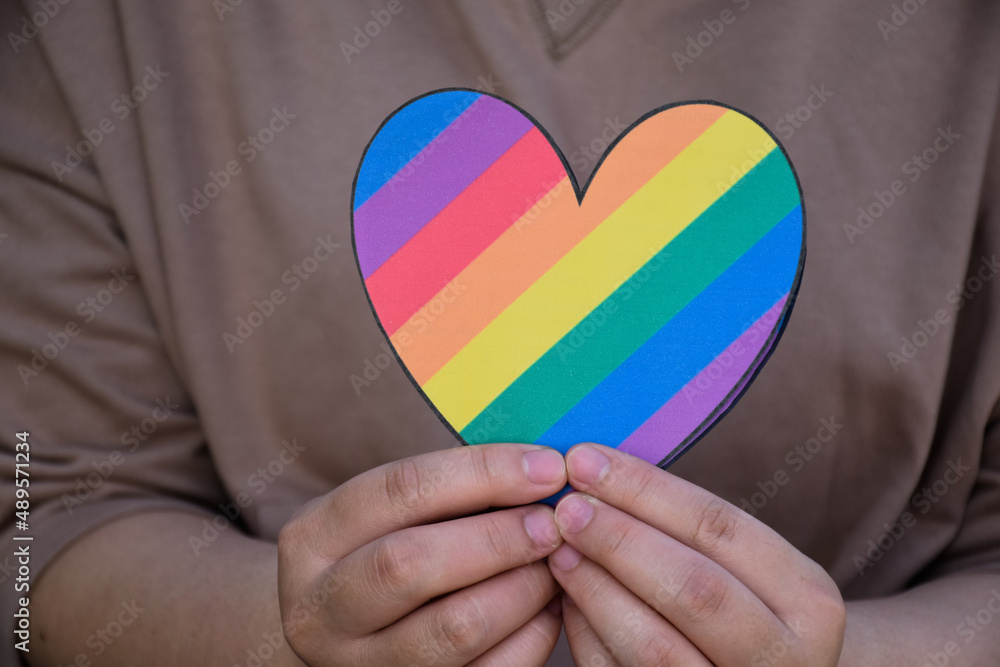 Two hearts made of rainbow colored paper are holding in hands of the LGBT person, concept for lgbtq+ communities celebrations in pride month around the world.