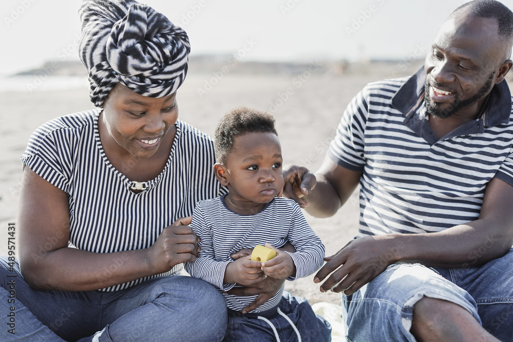 Happy african family having playful time together on the beach at summer vacation - Parents and child love concept