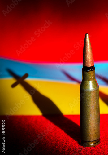 Obraz na płótnie Abstract image with a bullet from a machine gun and a shadow in the form of a grave cross on the background of the flag of Ukraine. (War in Ukraine - concept) w salonie