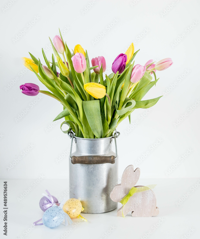 pink, yellow and purple tulips in silver metal milk can with easter eggs and wooden easter bunny 