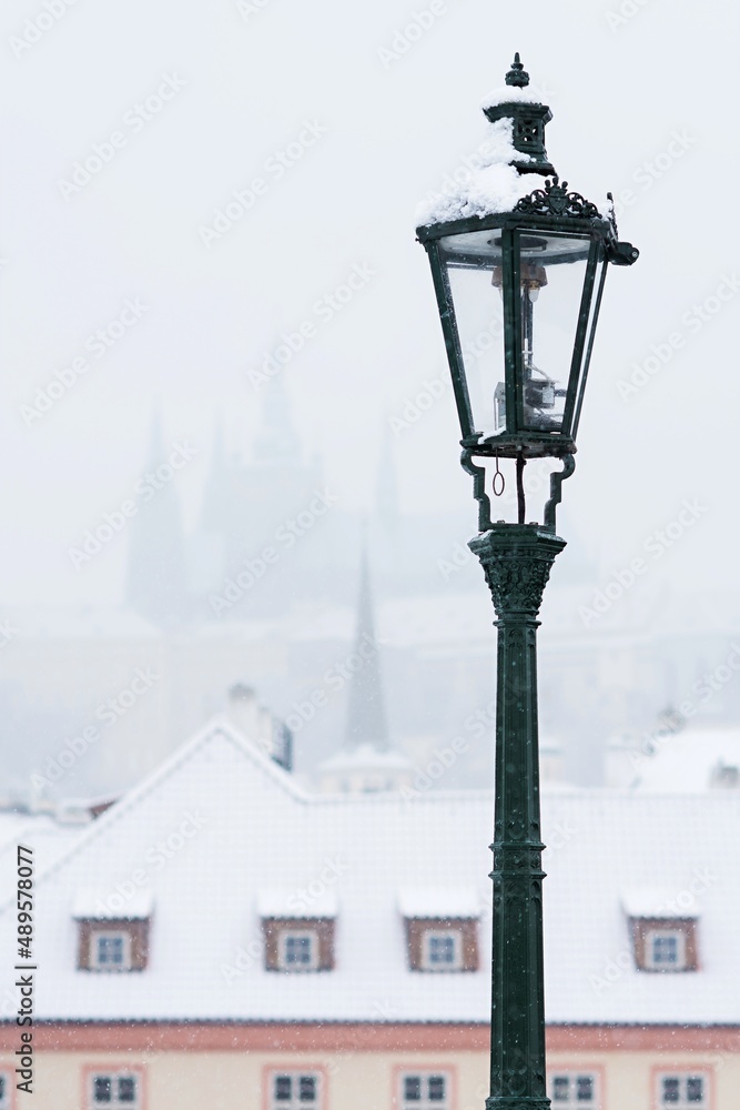 Street lamp in snowy Prague. In the background snow-covered houses and Prague Castle. Christmas atmosphere.
