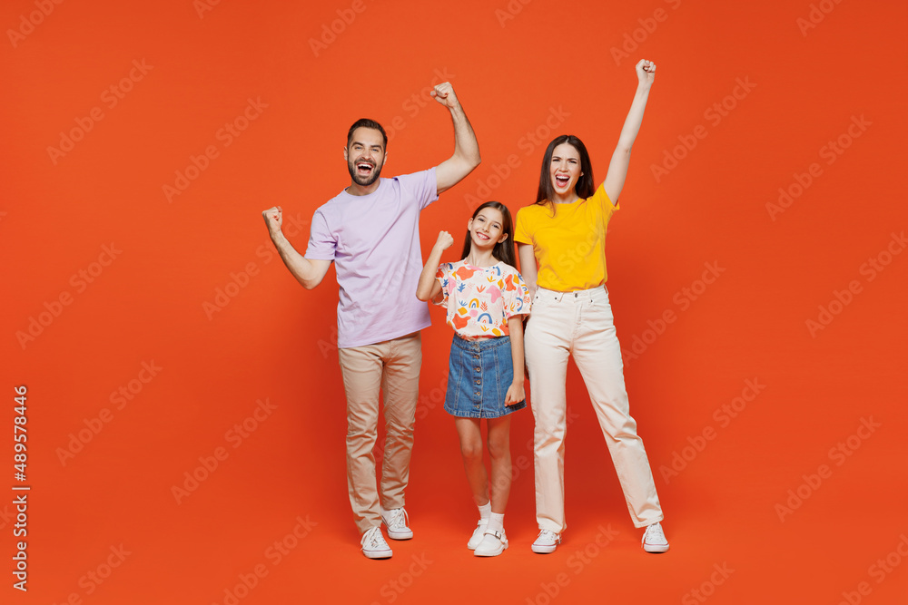 Fototapeta premium Full size young cool happy parents mom dad with child kid daughter teen girl wear basic t-shirts doing winner gesture celebrate isolated on yellow background. Family day parenthood childhood concept
