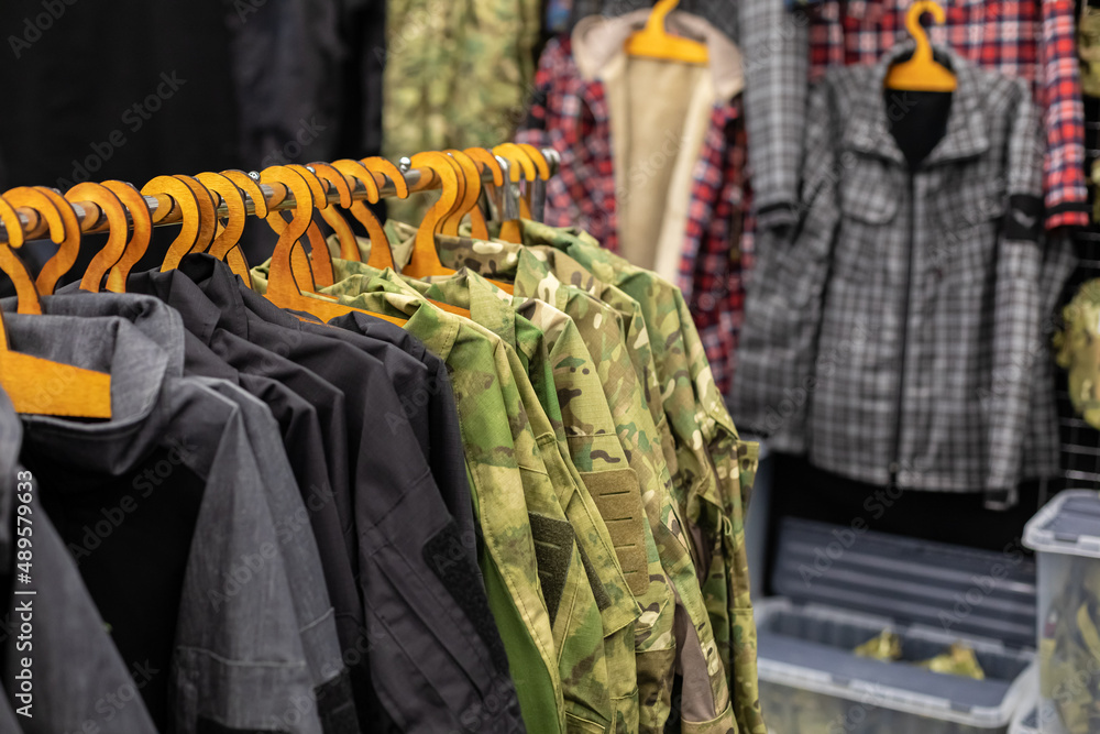 Department in the men's military clothing store. Camouflage uniforms hang on hangers in a
