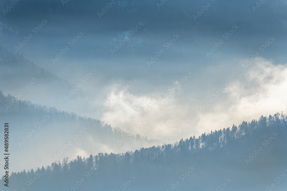 Fototapeta premium Silhouette of mountains in the mist above the sea of fog in winter.