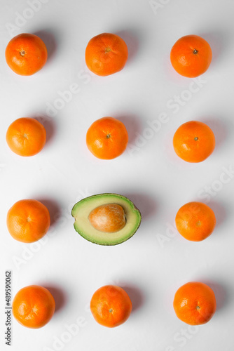 eleven oranges and one avocado on a gray background