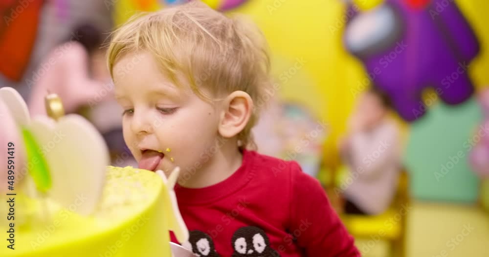 A little birthday boy bites a birthday cake prepared for his birthday. Boy surrounded by family and friends. Birthday party A little birthday boy bites a birthday cake prepared for his birthday. Boy surrounded by family and friends. Birthday party