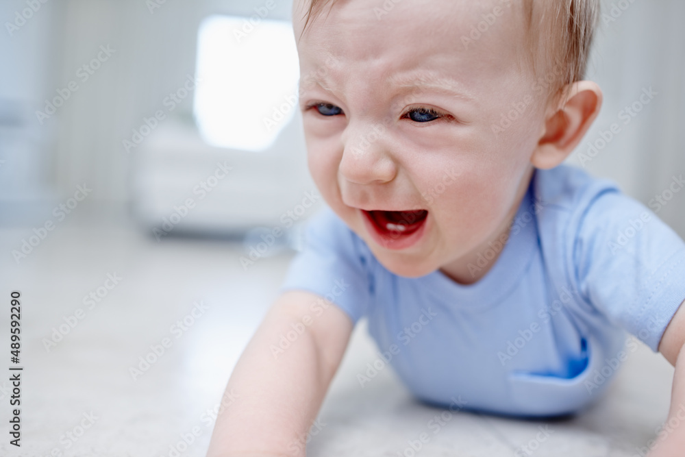 Teething is not fun. Closeup of a very unhappy baby boy lying on the floor.
