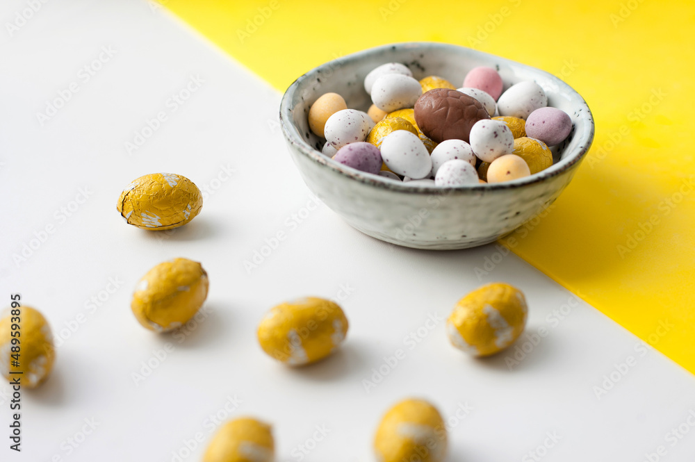 Easter colorful flat lay. Easter chocolate eggs of vibrant colors on bright yellow and white background. Culture food and easter celebration. Easter colorful flat lay. Easter chocolate eggs of vibrant colors on bright yellow and white background. Culture food and easter celebration.