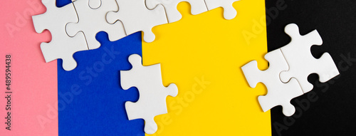 Missing jigsaw puzzle pieces. Business concept. Fragment of a folded white jigsaw puzzle and a pile of uncombed puzzle elements against the background of a colored surface.