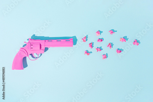 Pink pistol shoots popcorns on pastel blue background. Candy colors. Minimal flat lay concept of non-violence and peaceful conflict resolution. 