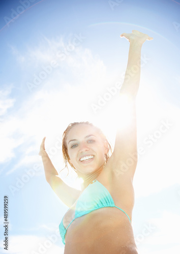 Young woman in bikini excited about her summer vacation. Happy young bikini woman with hands raised against the sunny sky.