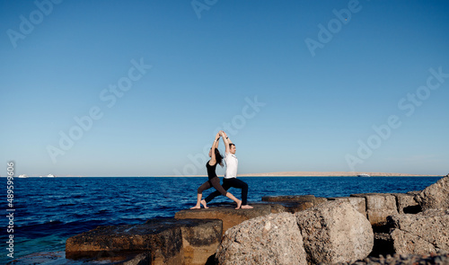 Couple sporty people practice yoga in pair, man and woman asana background blue sky and sea