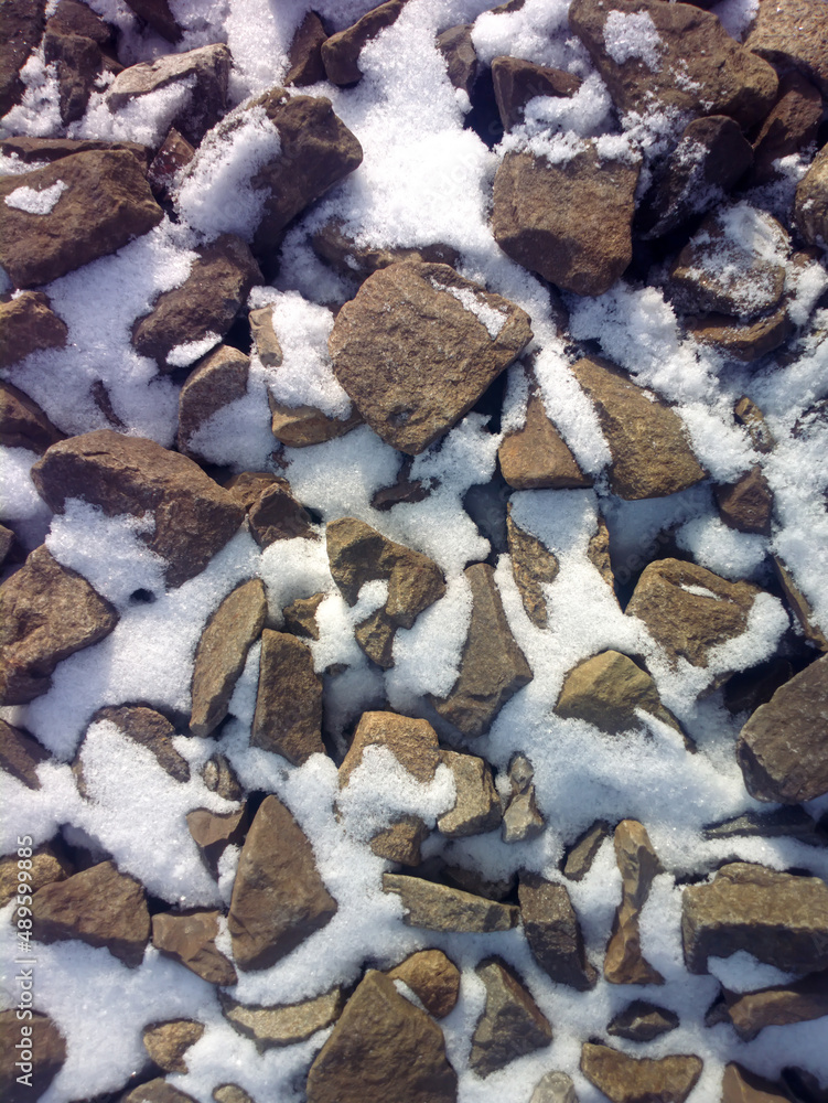 Fototapeta premium The texture of large stones with snow. Background of cobblestones.