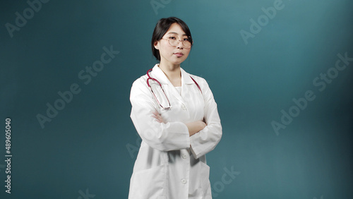 A serious doctor in a medical uniform is crossing her arms and looking at the camera