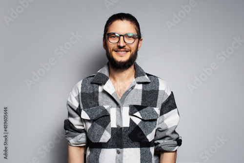Studio portrait of young smiling man in plaid shirt on grey background.