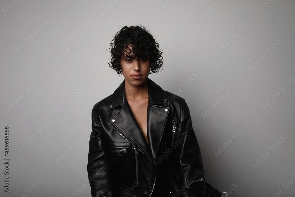 Obraz premium Young confident woman wears biker jacket looking at the camera on white wall.