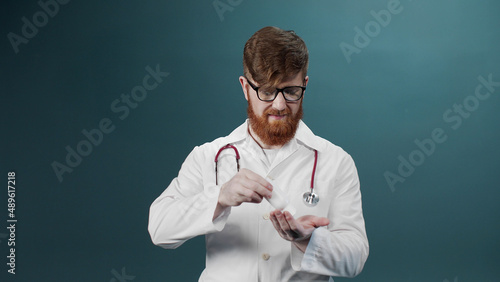 A man in a white medical gown cleans his hands with alcohol