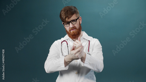 A man in a white medical gown and eyeglasses is sanitizing his hands and looking at the camera