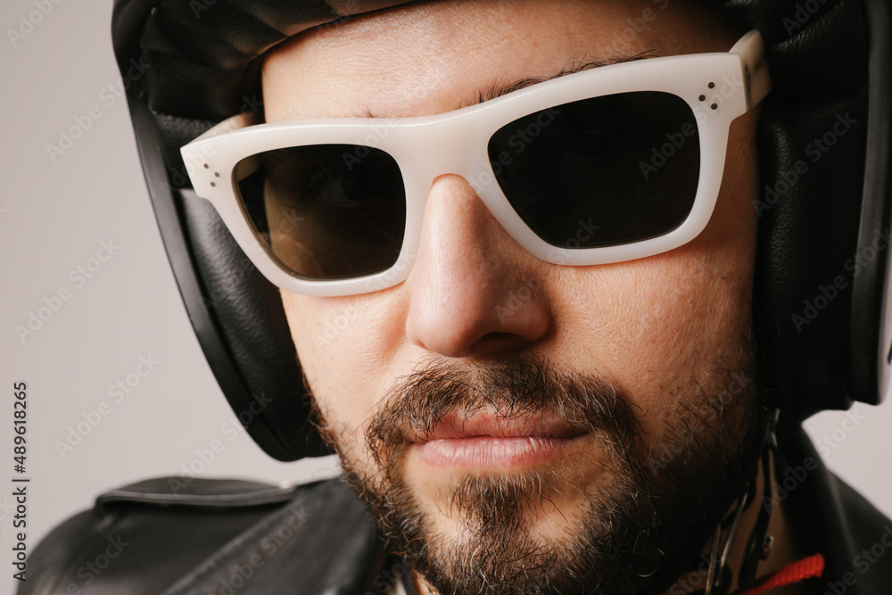 Fototapeta premium Close-up headshot of bearded biker man posing in leather jacket and sunglasses.