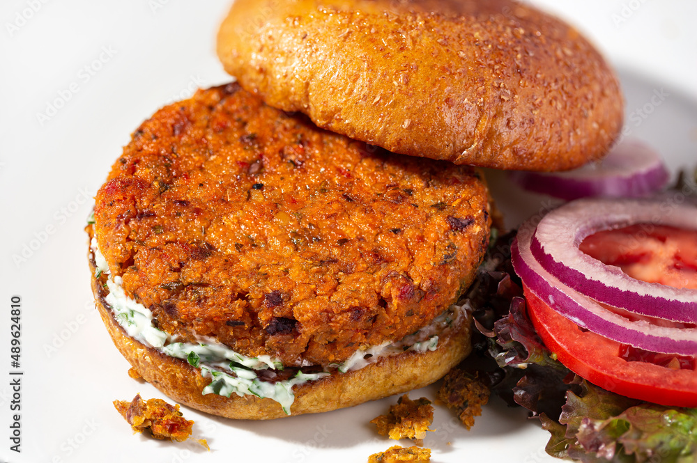 Chickpea veggie burger on a whole grain brioche bun with lettuce, tomato and onion on the side Chickpea veggie burger on a whole grain brioche bun with lettuce, tomato and onion on the side