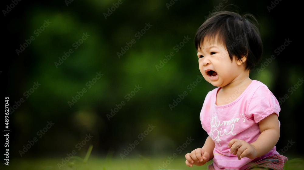 Cute baby Thai girl moody, crying and screaming , baby sitting on the grass in the park Cute baby Thai girl moody, crying and screaming , baby sitting on the grass in the park