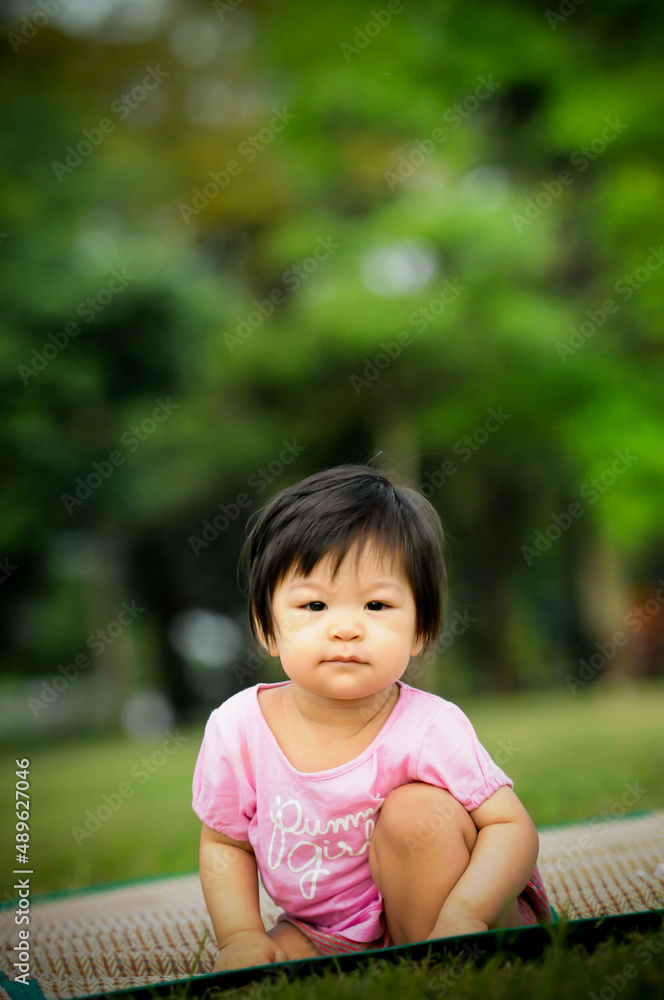 Cute baby Thai girl feel happy and relaxing , sitting on the grass in the park Cute baby Thai girl feel happy and relaxing , sitting on the grass in the park