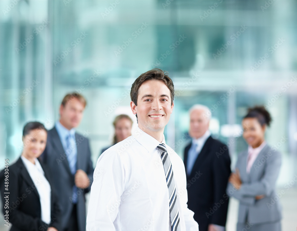 Im surrounded by excellent corporate role models. Handsome young business associate smiling with his colleagues in the background - portrait. Im surrounded by excellent corporate role models. Handsome young business associate smiling with his colleagues in the background - portrait.