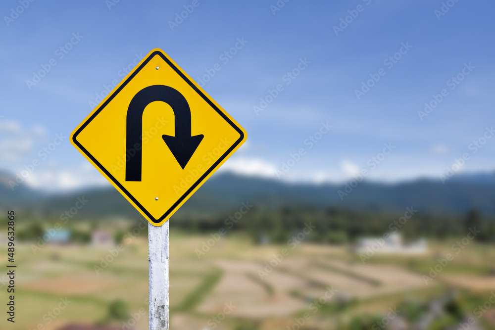 Traffic sign: Right U-turn sign on cement pole beside the rural road with white cloudy bluesky background, copy space. Traffic sign: Right U-turn sign on cement pole beside the rural road with white cloudy bluesky background, copy space.