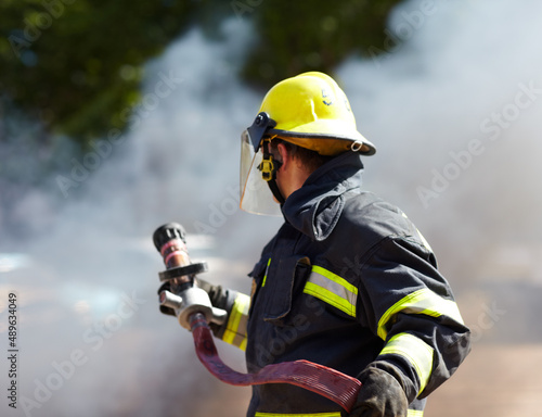 Hes got the situation under control. A caucasian fireman holding a hose and surrounded by the smoke from the fire hes just extinguished. photo