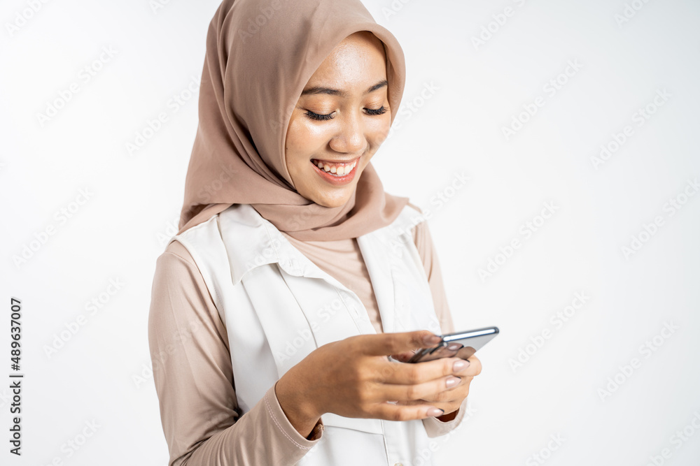 asian woman in hijab smiling while using a cell phone asian woman in hijab smiling while using a cell phone