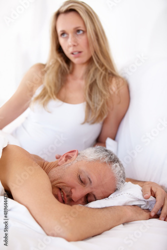 Dissatisfied partner. A woman sitting up in bed with dissatisfied expression while her husband sleeps.