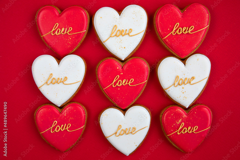 Nine red and white heart cookies with the inscription love on valentine's day on a red background. Symbol of love. View from above. Sweet dessert for the holiday. 