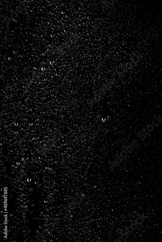Drops of water flow down the surface of the clear glass on a black background. Texture for creativity. Vertical placement of the frame. 