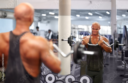 Looking good. Shot of a male bodybuilder looking in the mirror while lifting weights at the gym.