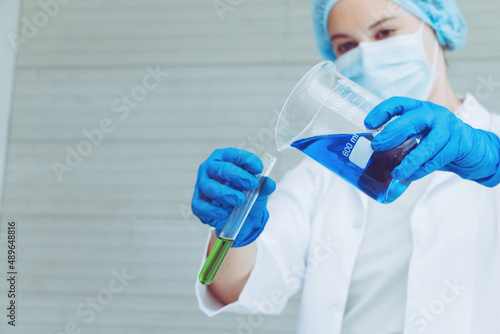 Scientist in uniform holding beaker and test tube have chemical liquid for testing chemical reaction.