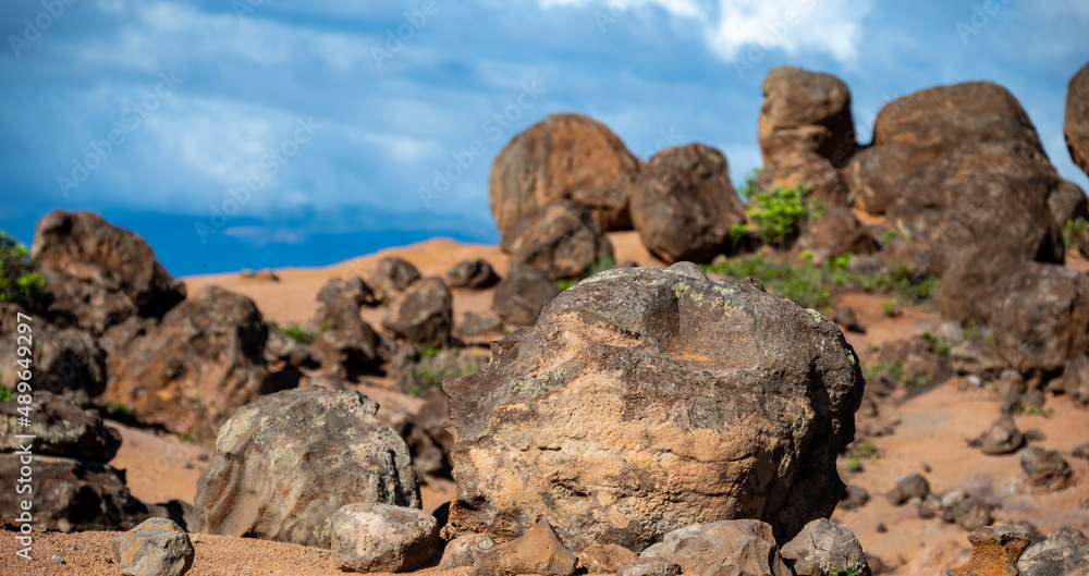 A scene of boulders and rocks on a hill of red clay dirt, blue sky above, in this rugged scene of the Garden of the Gods on the island of Lanai, Hawaii. 