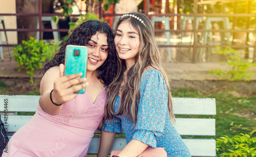 Two pretty girls sitting on a bench taking a selfie, girls smiling and taking a selfie, sisterly friendship concept photo