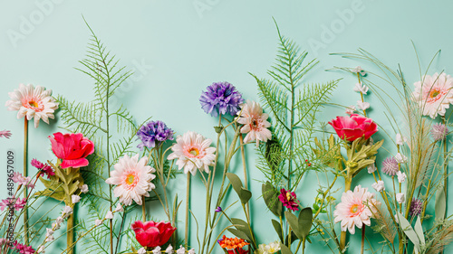 Various field flowers and fresh leaves in a row on pastel green background. Creative floral spring bloom concept. Still life natural visual trend idea. Flat lay.