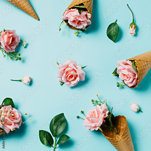 Pattern made with roses, ice cream cones and leaves on pastel blue background. Creative floral spring bloom concept. Still life natural visual trend. Trendy summer dessert or food idea. Flat lay.