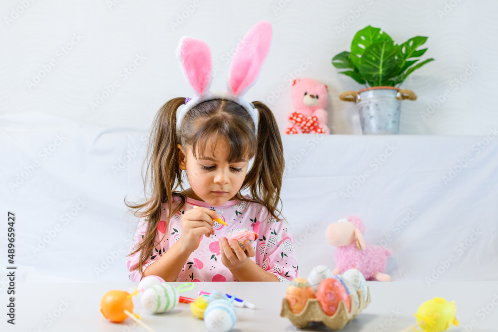 Happy little girl with bunny ears painting the egg with fiberpen, preparing for Happy Easter day. Preparing handmade . Happy little girl with bunny ears painting the egg with fiberpen, preparing for Happy Easter day. Preparing handmade .