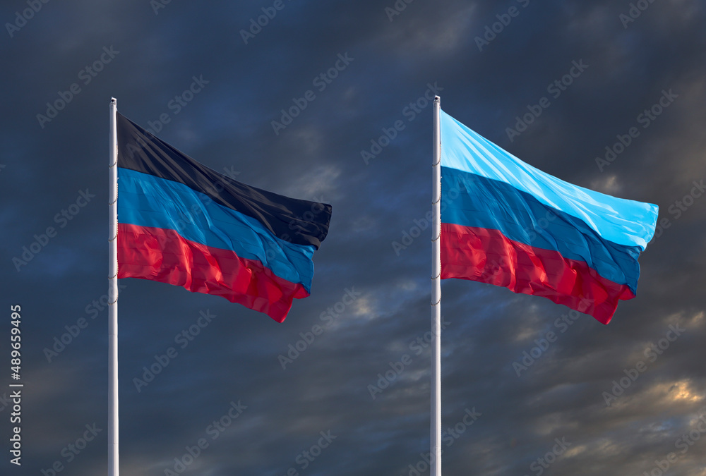 Flags of the Donetsk and Lugansk People's Republics against a dark cloudy sky.