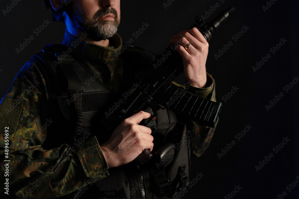 Fototapeta premium Close-up of soldier in military uniform with weapon on black background.